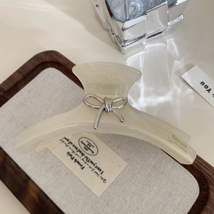 Détail de la pince à cheveux en acétate crème avec nœud argenté et texte Barrette