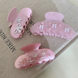 Three elegant pink acetic acid hair claws with rhinestone and bow accents on linen background
