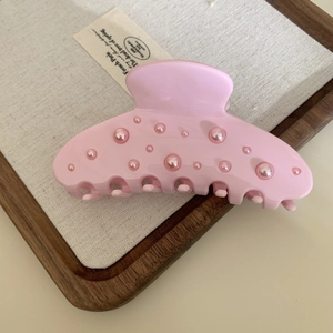 Close-up of pink acetate hair claw clip with faux pearl embellishments on a tray