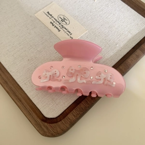 Detailed view of pink acetate hair claw with white bows and sparkling rhinestones