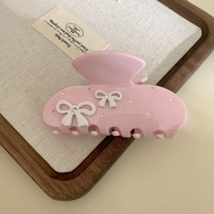 Detail of pink acetate hair claw clip featuring white bows and sparkling rhinestones
