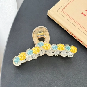 Close-up of a large clear acrylic hair claw clip with five bright yellow pineapple motifs
