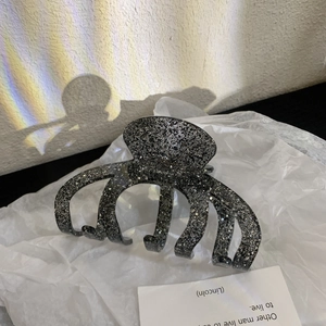 Close-up of a large black hair claw clip with shimmering silver glitter and a multi-tooth design