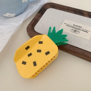 Detailansicht einer gelben Ananas-Haarklammer mit grünen Blättern auf einem Holztablett