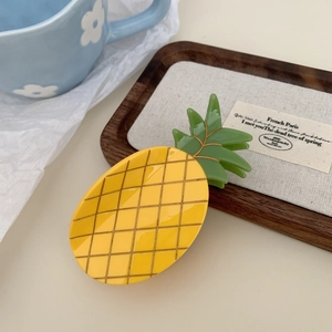 Detailaufnahme einer gelben Ananas-Haarklammer auf einem Schmucktablett aus Holz