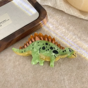 Close-up of a green acetate hair claw clip in stegosaurus dinosaur shape with orange spikes