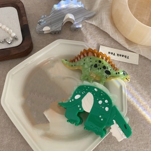 Detailed close-up of acetate dinosaur hair claw clips in a stylish ceramic tray