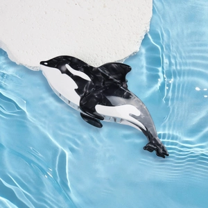 Dettaglio della molletta per capelli a forma di orca in acetato su fondo d'acqua blu