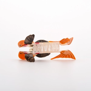 Dettaglio di una molletta per capelli a forma di pesce in acetato arancio e bianco