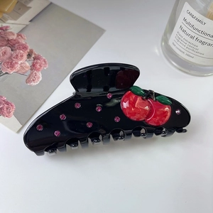 Détail d'une pince à cheveux noire avec cerises 3D et strass roses sur fond blanc