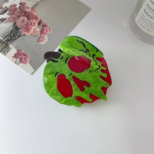 Détail macro de la pince à cheveux en acétate avec motif de tête de mort et pomme empoisonnée
