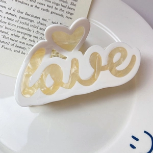 Détail d'une pince à cheveux en acétate blanc avec lettrage LOVE et motif de cœur