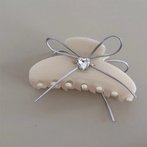 Detail of a cream acetate hair claw featuring a silver ribbon bow and a heart zircon