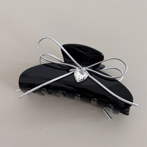 Detail of black acetate hair claw with silver ribbon bow and heart-shaped gemstone