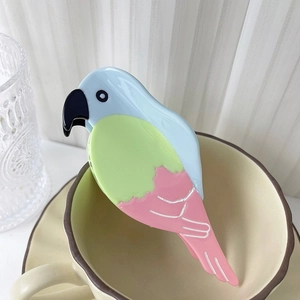 Vue détaillée de la pince à cheveux perroquet en bleu pastel et vert sur une tasse