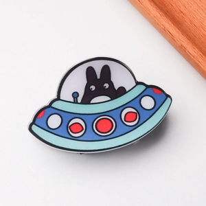 Detailed view of an alien UFO enamel pin featuring a black cartoon character on white