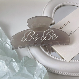 Detail of grey acetate hair claw clip with pearl Be Be lettering on blue background