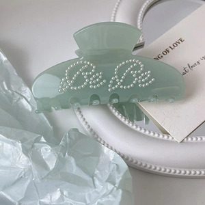 Detail of light green acetic acid hair claw clip with white pearls spelling Bebe