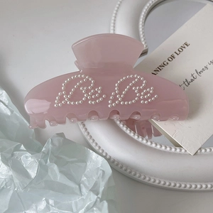 Detailed close-up of light pink acetate hair claw with Be Be pearl letter inlay