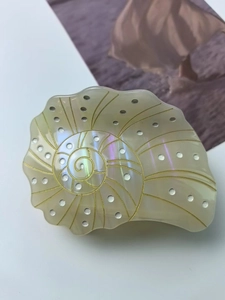 Macro detail of iridescent shell hair claw clip with golden spiral patterns and pearl finish