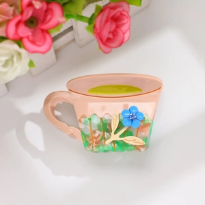 Détail de la pince à cheveux en forme de tasse pêche avec fleur bleue et motif acétate