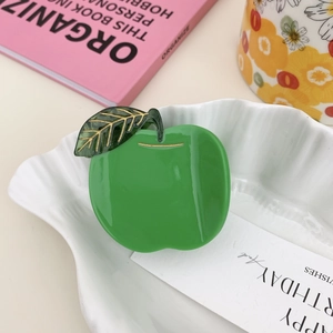 Close-up of green apple hair claw clip with golden veins and polished finish in a white bowl
