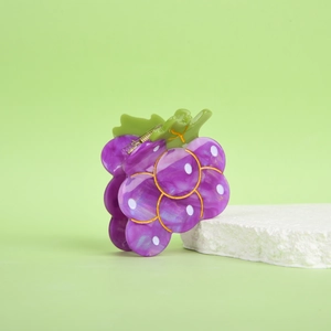 Dettaglio della molletta per capelli a uva viola con texture marmorea e foglia verde