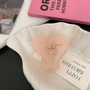 Détail d'une pince à cheveux en forme de cœur rose pastel sur un plateau en coquillage