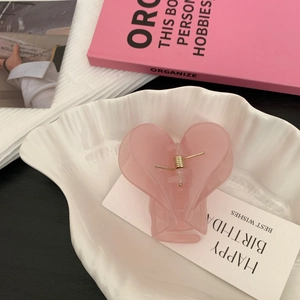 Détail d'une pince à cheveux en forme de cœur rose sur un plateau en coquillage