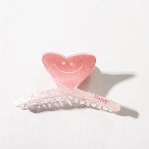 Macro detail of a pink heart-shaped acetate hair claw with a smile and Happy text