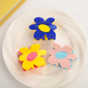 Three elegant acetate flower hair claws in blue, yellow, and pink colors on a white plate