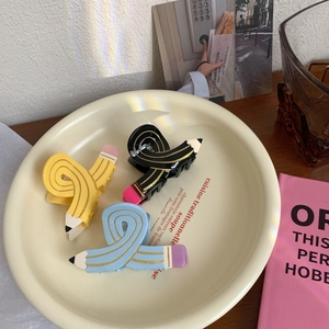 Creative pencil shaped hair claws in yellow black and blue on a decorative ceramic plate