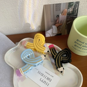 Unique pencil shaped hair claw set in yellow, blue and black on a decorative tray