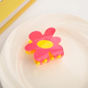 Detail of flower-shaped pink hair claw clip with yellow center on white ceramic plate