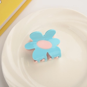 Detailed close-up of light blue flower claw clip with pink center on white ceramic plate