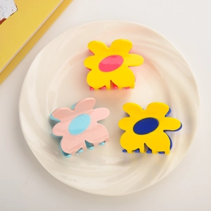 Three colorful acetate flower hair claws set on a white ceramic plate with a yellow book