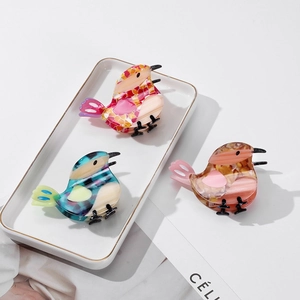 Three bird-shaped acetate hair claws with marble and floral patterns on a ceramic tray