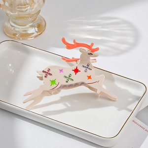 Detail of cream reindeer hair claw clip with colorful star rhinestones and orange antlers