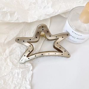 Detail of star-shaped hair claw with matte bronze finish and elegant black polka dots