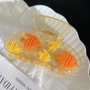 Detailopname van gele visvormige haarklem van acetaat op een decoratieve schelpen tray