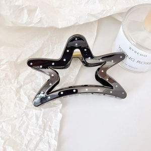 Detailed top view of black star-shaped hair claw clip with white dots on textured paper