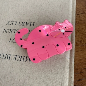 Close-up of pink cat hair claw clip with black polka dots on a decorative book