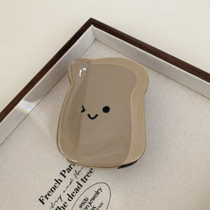 Detail of a toast-shaped hair claw clip with a winking cartoon face and glossy resin finish