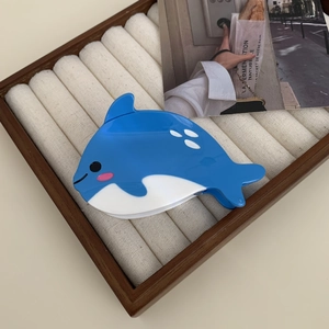 Détail d'une pince à cheveux en forme d'orque bleue et blanche sur un plateau à bijoux en bois