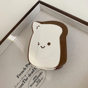 Close-up of a toast-shaped ceramic jewelry tray featuring a minimalist winking smiley face