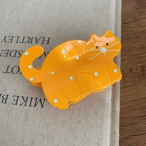 Close-up of orange cat-shaped hair claw clip with white polka dots and metal spring