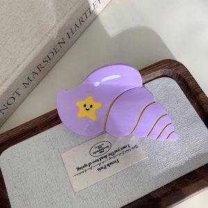 Gros plan d'une pince à cheveux coquillage violet avec étoiles jaunes sur plateau