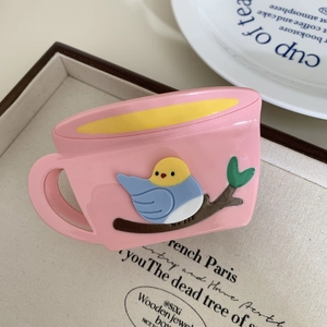 Rosa Haarklammer in Kaffeetassen-Form mit Vogel-Motiv auf beigem Canvas-Hintergrund