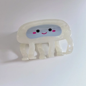 Macro detail of cartoon pufferfish hair claw clip with eyes and pink blush on cream finish