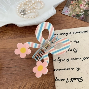 Detail of pink and blue striped bow hair claw clip with floral accents on wood
